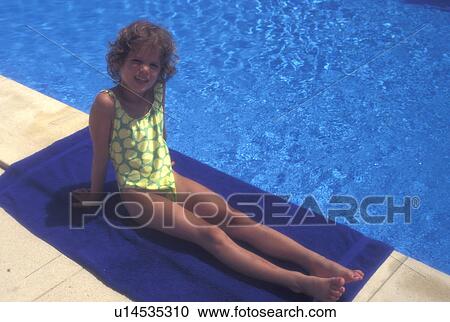 Stock Image -  swimming pool, Switzerland, Vaud, Rolle, La Cote, A 6 year old girl sits on a blue towel next her swimming pool at home in Rolle in the Canton of Vaud.. Fotosearch