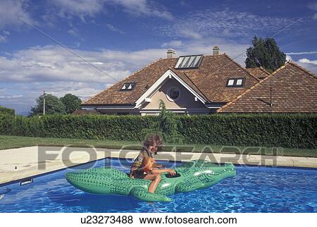 Stock Photo -  swimming pool, Switzerland, Vaud, Rolle, La Cote, A 6 year old girl floats on an inflatable alligator in her swimming pool at home in Rolle in the Canton of Vaud.. Fotosearch