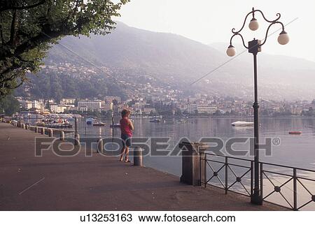 Stock Image -  Switzerland, Ticino, Locarno, Woman standing on the lakefront of Lake Maggiore in the city of Locarno.. Fotosearch