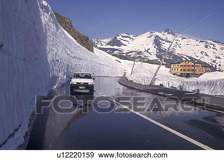Stock Photo -  Switzerland, Valais, Alps, Grimsel Pass, Snow piled high next to the mountain road leading to the Grimsel-Blick Hotel-Restaurant in the summer on the summit of Grimsel Pass the Swiss Alps in the Canton of Valais.. Fotosearch