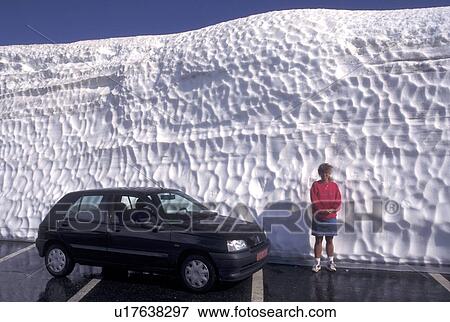 Switzerland, Valais, Alps, Grimsel Pass, Woman standing by her car look small next to a huge snow drift on the summit of Grimsel Pass the Swiss Alps in the Canton of Valais in the summer (July). View Large Photo Image Stock Photo - Switzerland, Valais, Alps, Grimsel Pass, Woman standing by her car look small next to a huge snow drift on the summit of Grimsel Pass the Swiss Alps in the Canton of Valais in the summer (July).. Fotosearch