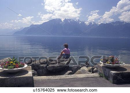 Vevey, Switzerland, Vaud, Lake Geneva, Alps, Woman sitting on a rock looking out at the scenic view of Lac Leman and the Alps from a lakefront park in Vevey in the Canton of Vaud. View Large Photo Image Stock Photography - Vevey, Switzerland, Vaud, Lake Geneva, Alps, Woman sitting on a rock looking out at the scenic view of Lac Leman and the Alps from a lakefront park in Vevey in the Canton of Vaud. . Fotosearch
