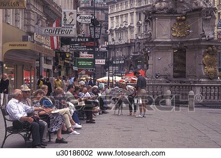 Stock Image -  Vienna, Austria, Wien, People sitting on bench in the plaza on Graben Street in downtown Vienna.. Fotosearch