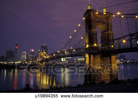 Stock Photography -  Cincinnati, OH, Ohio, John A. Roebling Bridge, downtown skyline along the Ohio River, evening. Fotosearch