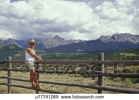 Stock Photo -  CO, Colorado, San Juan National Forest, San Juan Mountains, Mount Sneffels Wilderness, San Juan Skyway, Woman on fence. Fotosearch