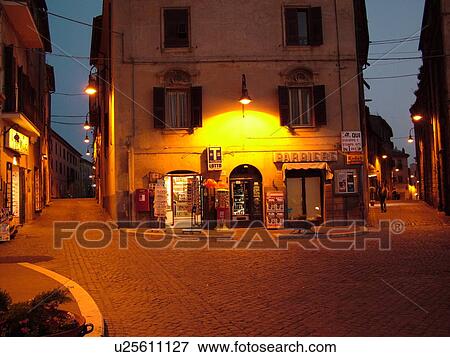 Stock Photo -  Lazio, Tarquinia, Italy, Europe, Shops along the street in the medieval town of Tarquinia in the evening.. Fotosearch