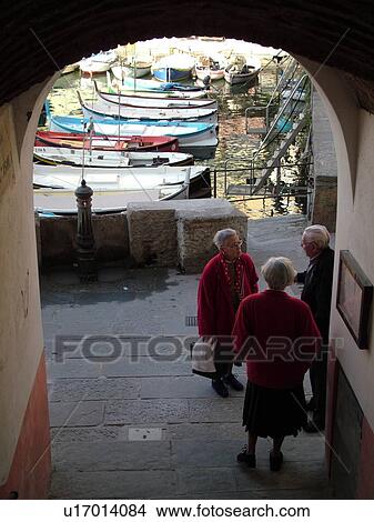 Liguria, Italy, Camogli, Riviera di Levante, Ligurian Riviera, Europe, Local elderly Italian people talking together through an archway along the waterfront of the fishing port in the resort town of Camogli along the Ligurian Sea. View Large Photo Image Picture -  Liguria, Italy, Camogli, Riviera di Levante, Ligurian Riviera, Europe, Local elderly Italian people talking together through an archway along the waterfront of the fishing port in the resort town of Camogli along the Ligurian Sea.. Fotosearch