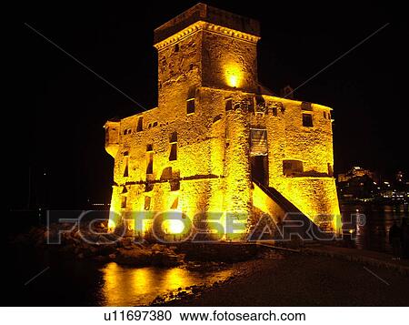 Stock Image -  Liguria, Italy, Rapallo, Riviera di Levante, Ligurian Riviera, Europe, The Fortress illuminated at night on the Gulf of Tigullio (Gulfo di Tigullo) in the resort town of Rapallo along the Ligurian Sea on the Ligurian Riviera.. Fotosearch