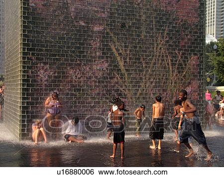 Stock Photograph -  Chicago, IL, Illinois, Windy City, Downtown, Millennium Park, Crown Fountain, children cooling off, hot summer day, video image on wall, mural. Fotosearch