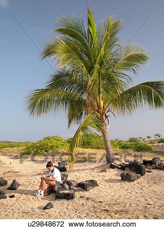 Stock Image -  Kailua-Kona, Big Island, Island of Hawaii, HI, Hawaii, Kona Coast, Leeward, West Coast, Old Kona Airport State Recreation Park, woman reading a book on the beach. Fotosearch