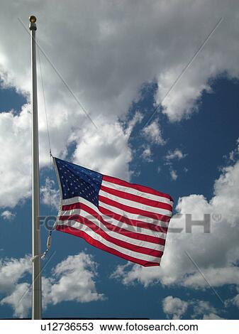 Stock Image -  Montpelier, VT, Vermont, American Flag, flag pole, flying half mast against a blue sky with white puffy clouds. Fotosearch