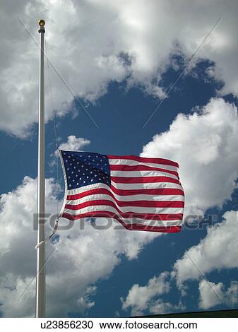 Stock Image -  Montpelier, VT, Vermont, American Flag, flag pole, flying half mast against a blue sky with white puffy clouds. Fotosearch