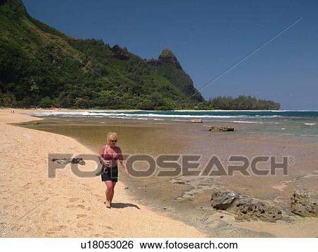 Stock Photograph -  Napali Coast, Kauai, HI, Hawaii, North Shore, Na Pali, Haena Beach Park, Tunnels Beach, woman walking on the beach. Fotosearch