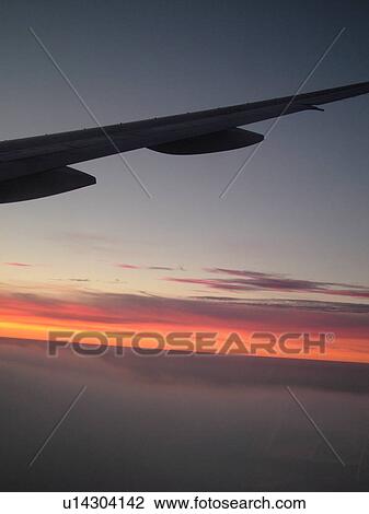 Stock Image -  aerial, plane flying above the clouds, wing, sunrise. Fotosearch