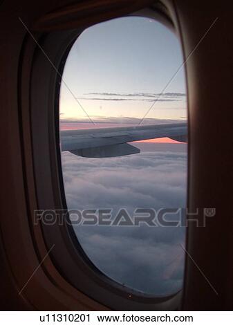 Stock Image -  aerial, view of plane flying above the clouds from the window, wing, sunrise. Fotosearch