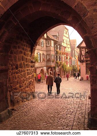 Stock Image -  France, Europe, Alsace, Riquewihr, Haut-Rhin, L'Alsace Wine Region, Route du Vin, downtown, archway, cobblestone pedestrian street, half-timbered buildings. Fotosearch