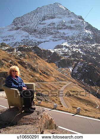 Stock Image -  Switzerland, Europe, Bern, Berne, Sustenpass, Susten Pass, Berner Oberland, switchback, woman sitting in a chair at the pass, mountain road, humor. Fotosearch