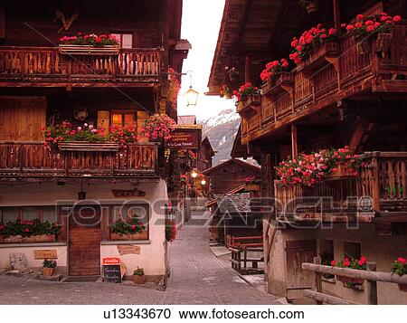 Stock Image -  Switzerland, Europe, valais, wallis, Val d'Anniviers, Grimentz, old chalets along a narrow pedestrian street decorated with flowers. Fotosearch