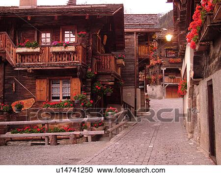 Stock Image -  Switzerland, Europe, valais, wallis, Val d'Anniviers, Grimentz, old chalets along a narrow pedestrian street decorated with flowers. Fotosearch
