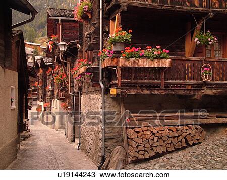 Stock Image -  Switzerland, Europe, valais, wallis, Val d'Anniviers, Grimentz, old chalets along a narrow pedestrian street decorated with flowers. Fotosearch