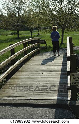 Stock Image -  West Chester, PA, Pennsylvania, Hershey's Mill Chester County, woman walking across a bridge, recreation path. Fotosearch