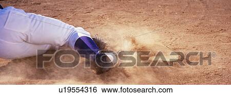 Stock Photograph - Low section of baseball player sliding towards base on field. Fotosearch