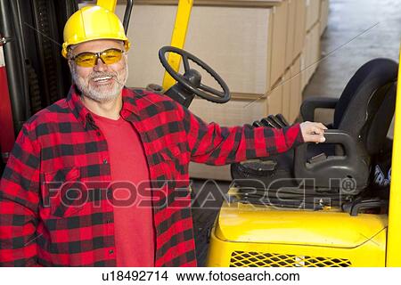 Picture - Man standing by fork lift truck smiling. Fotosearch