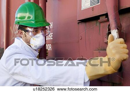 Stock Photograph - Worker in hazmat suit, hard-hat and face mask closing metal door. Fotosearch