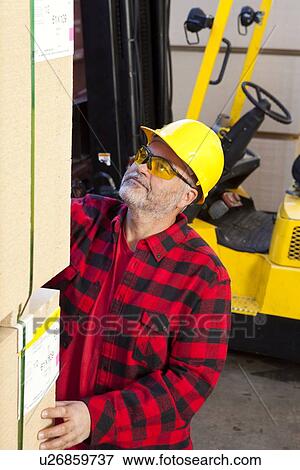 Stock Photo - Worker inspecting wood pallet standing by fork lift truck. Fotosearch