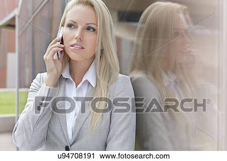 Beautiful blond businesswoman conversing on cell phone while looking away by glass wall View Large Photo Image Stock Image - Beautiful blond businesswoman conversing on cell phone while looking away by glass wall. Fotosearch