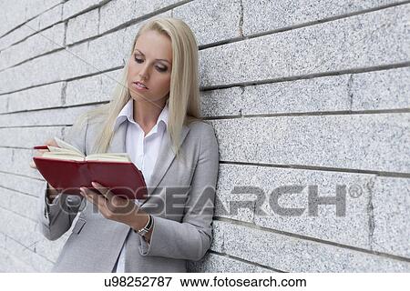 Beautiful young businesswoman reading notes in organizer while leaning on wall View Large Photo Image Stock Photo - Beautiful young businesswoman reading notes in organizer while leaning on wall. Fotosearch