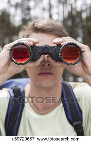 Close-up of young man looking through binoculars in forest View Large Photo Image Stock Photo - Close-up of young man looking through binoculars in forest. Fotosearch