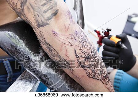 Stock Photo - Cropped image of artist tattooing man's arm in studio. Fotosearch