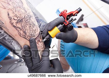 Cropped image of artist tattooing man's arm in tattoo parlor View Large Photo Image Stock Photograph - Cropped image of artist tattooing man's arm in tattoo parlor. Fotosearch