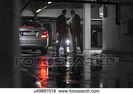 Full length of businessmen giving and receiving envelop in parking lot View Large Photo Image Stock Photo - Full length of businessmen giving and receiving envelop in parking lot. Fotosearch