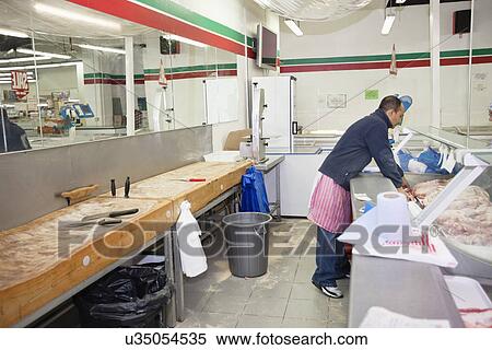 Stock Photography - Full-length of male employee organizing meat in supermarket. Fotosearch