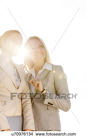 Picture - Happy young businesswomen looking away against sky. Fotosearch