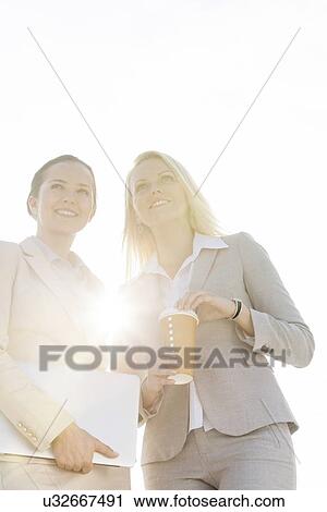 Happy young businesswomen with disposable cup and laptop against sky View Large Photo Image Stock Image - Happy young businesswomen with disposable cup and laptop against sky. Fotosearch