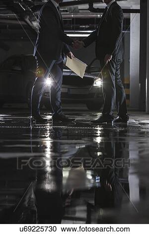 Stock Image - Low section of businessmen conducting suspicious business in parking lot. Fotosearch