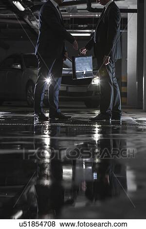 Stock Photo - Low section of businessmen giving and receiving briefcase in parking lot. Fotosearch