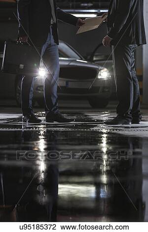 Stock Image - Low section of businesspeople conducting suspicious business in basement. Fotosearch