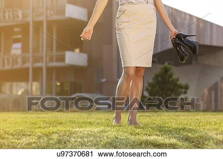 Low section of young businesswoman holding footwear in office lawn View Large Photo Image Stock Image - Low section of young businesswoman holding footwear in office lawn. Fotosearch