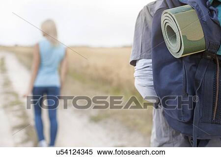 Male hiker carrying backpack with woman walking in foreground on field View Large Photo Image Stock Photography - Male hiker carrying backpack with woman walking in foreground on field. Fotosearch