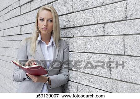 Portrait of beautiful businesswoman holding organizer while leaning on wall View Large Photo Image Stock Photo - Portrait of beautiful businesswoman holding organizer while leaning on wall. Fotosearch