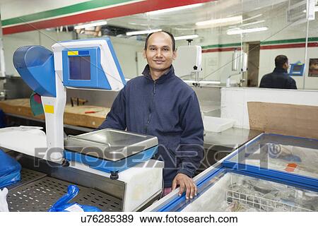 Stock Photo - Portrait of confident male employee standing in front on weighing machine at grocery store. Fotosearch