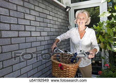 Portrait of happy senior woman with bicycle standing at backyard View Large Photo Image Stock Photo - Portrait of happy senior woman with bicycle standing at backyard. Fotosearch