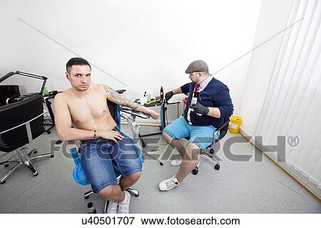 Stock Photo - Portrait of young man getting tattooed from artist in tattoo shop. Fotosearch