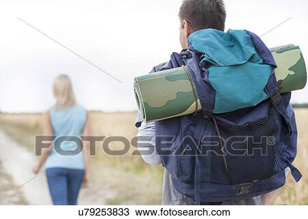 Rear view of male hiker carrying backpack with woman walking in foreground on field View Large Photo Image Stock Image - Rear view of male hiker carrying backpack with woman walking in foreground on field. Fotosearch