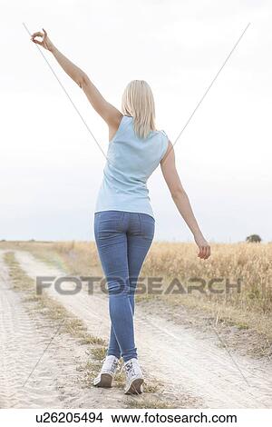 Picture - Rear view of young woman walking on trail at field. Fotosearch