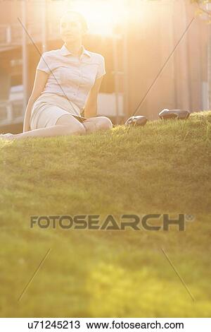 Stock Image - Relaxed young businesswoman sitting in office lawn. Fotosearch